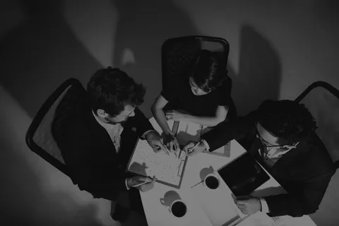 Three colleagues meeting to discuss charts over coffee.